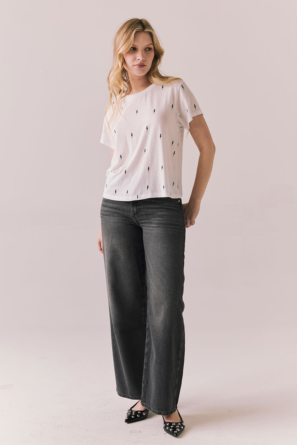 Full front view of model wearing the Tossed Bolts short sleeve tee in white with black scattered lightning bolt graphic and relaxed fit and  gray pants on a plain background