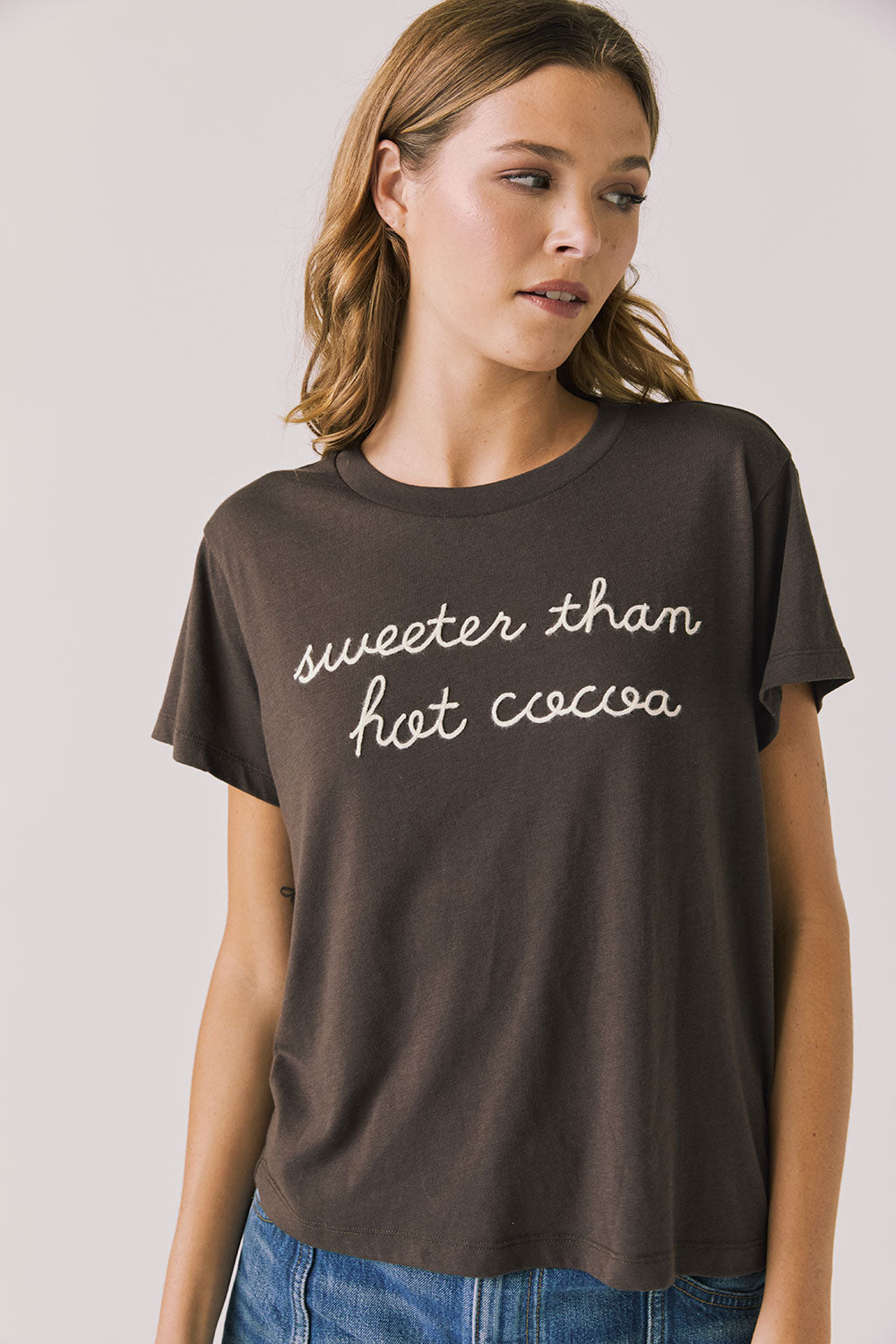 Front view of woman wearing Chaser’s brown Hot Cocoa Tee with “sweeter than hot cocoa” text on a plain background