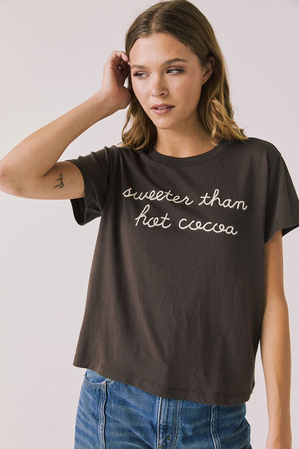 Front view of woman wearing Chaser’s brown Hot Cocoa Tee with “sweeter than hot cocoa” text on a plain background