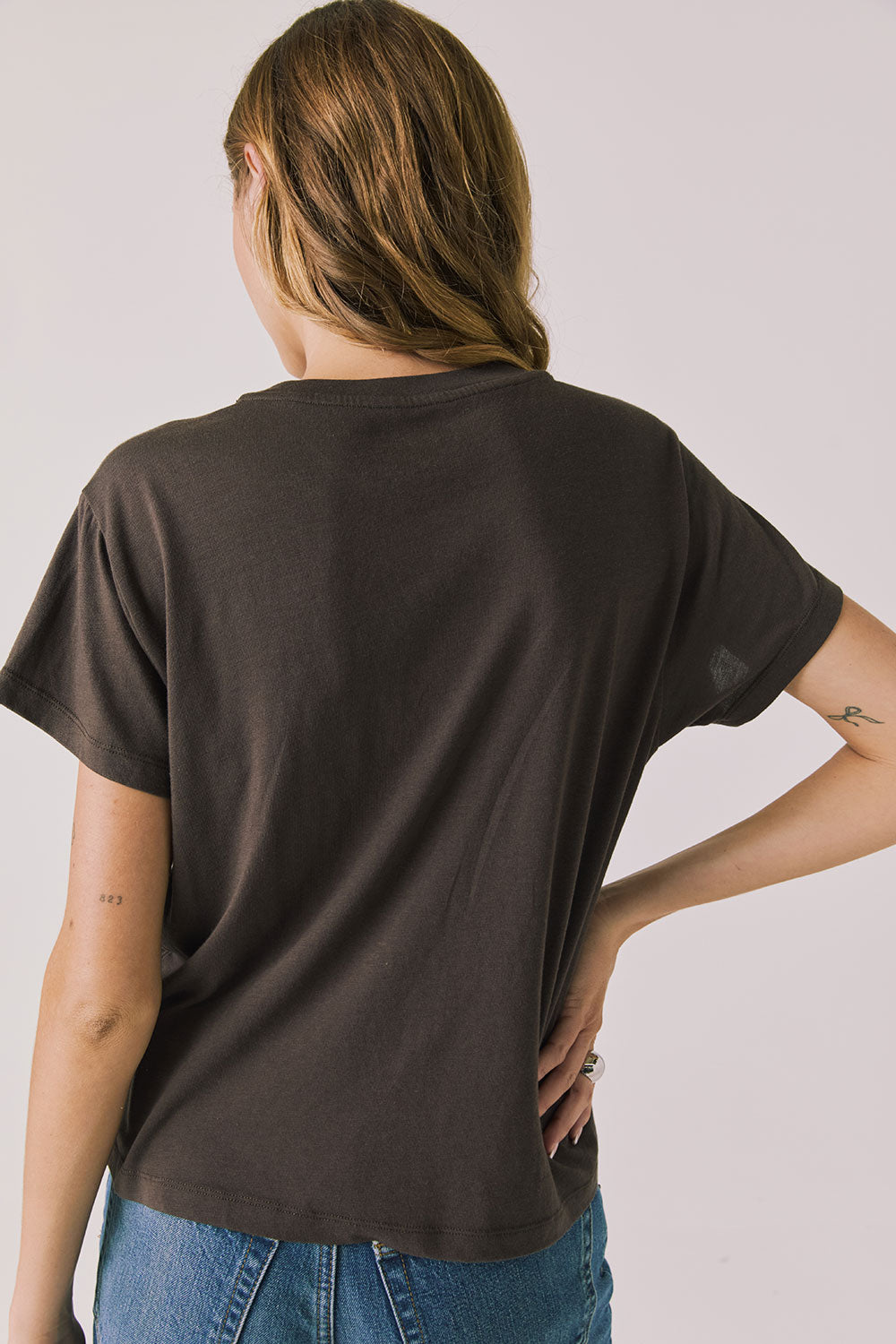 Back view of woman wearing Chaser’s brown Hot Cocoa Tee on a plain background