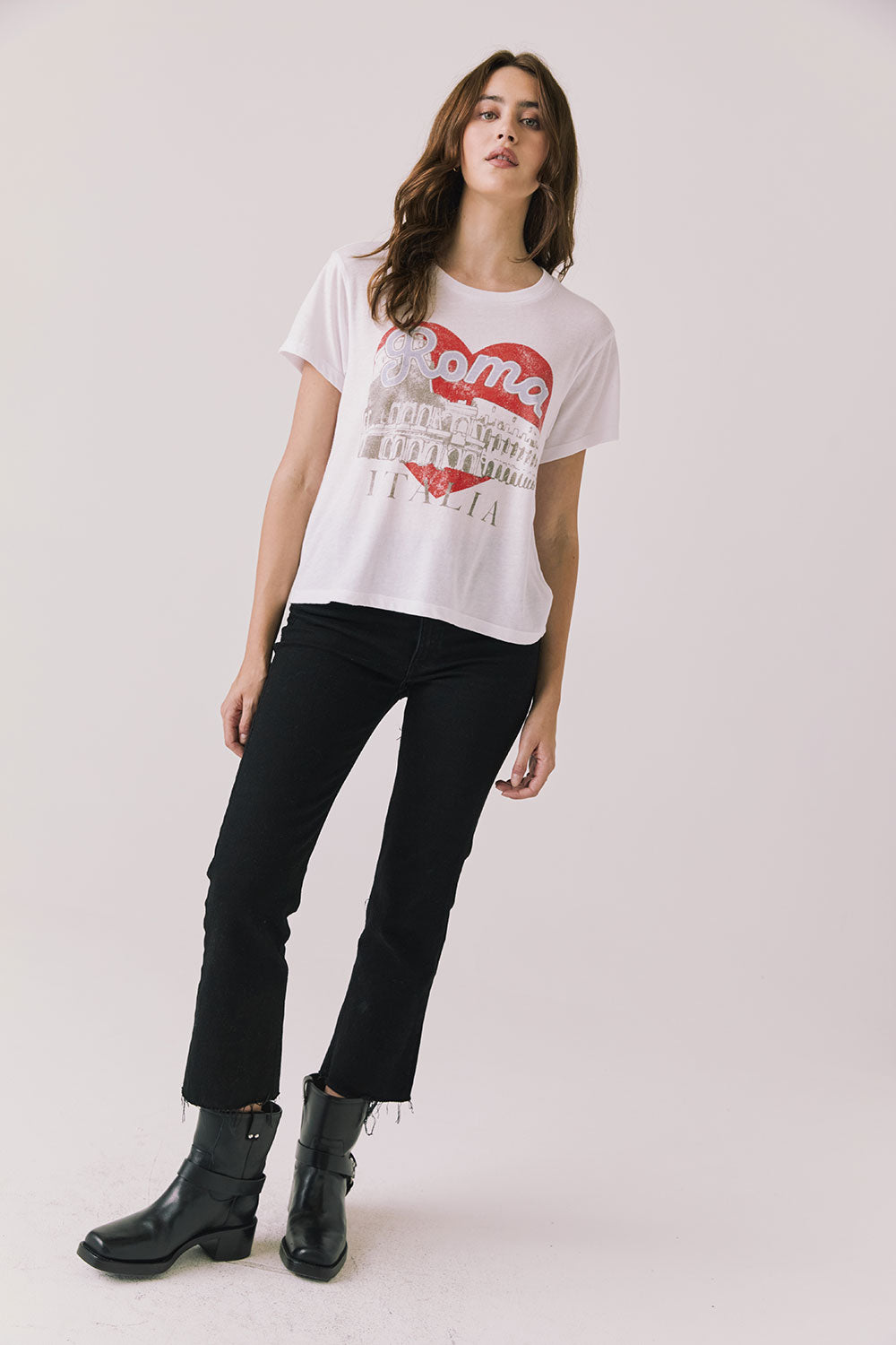 Full body view of woman wearing Chaser's white Italian slogan tee featuring red heart and Colosseum design, paired with black pants and black boots on a light background