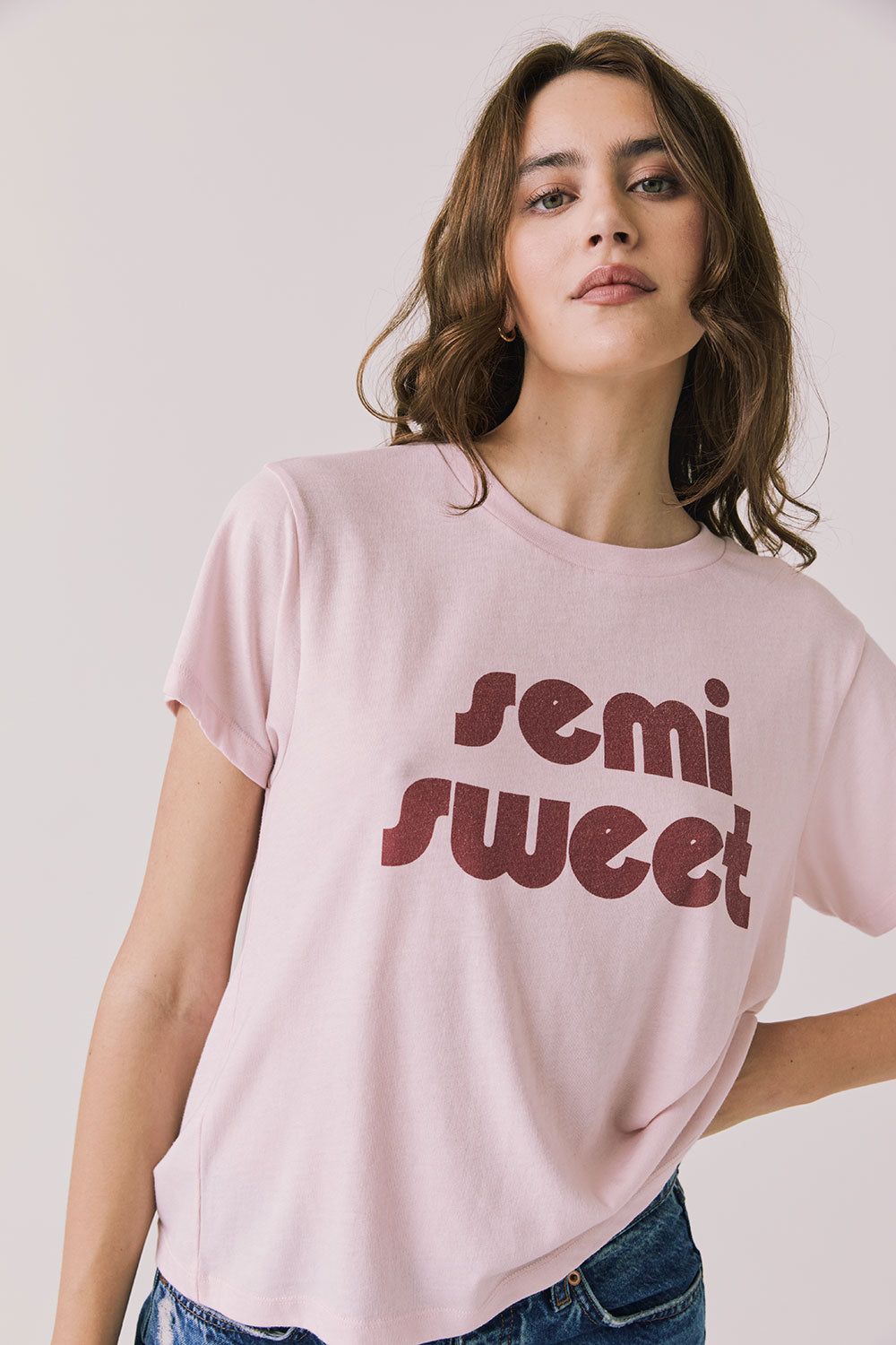 Front view of woman wearing Chaser’s Semi Sweet Pink Tee with “semi sweet” text on a light background