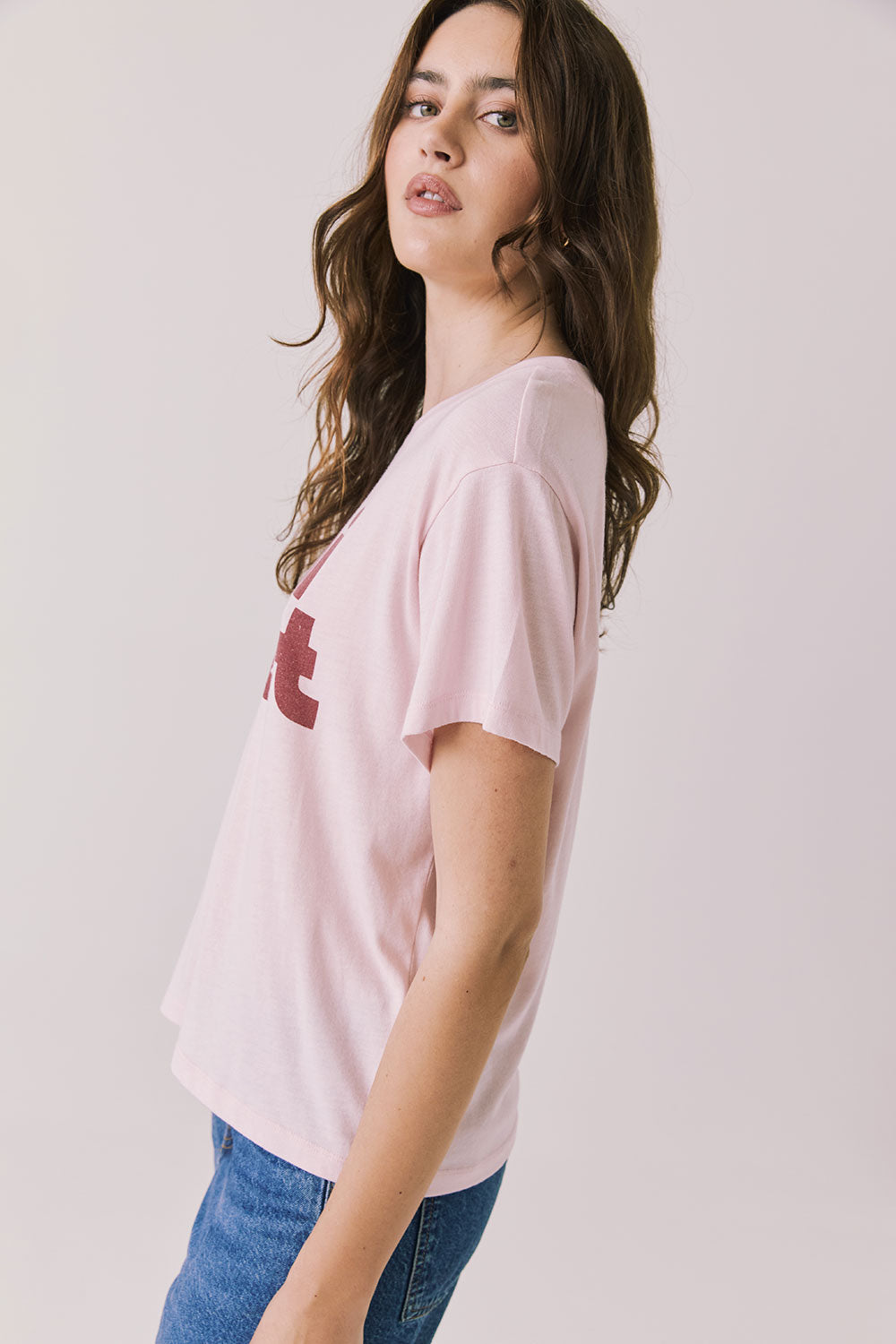 Side view of woman wearing Chaser’s Semi Sweet Pink Tee with “semi sweet” slogan detail on a light background