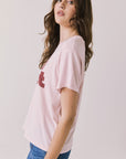 Side view of woman wearing Chaser’s Semi Sweet Pink Tee with “semi sweet” slogan detail on a light background