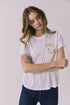 Front view of a woman wearing Chaser's white Apres Tennis Tee with text and graphics on a plain background
