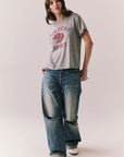 Full front view of model wearing Wildcat Spirit Tee in Heather Grey with maroon wildcat chest graphic with blue jeans, and white sneakers with red stripes on a light background.