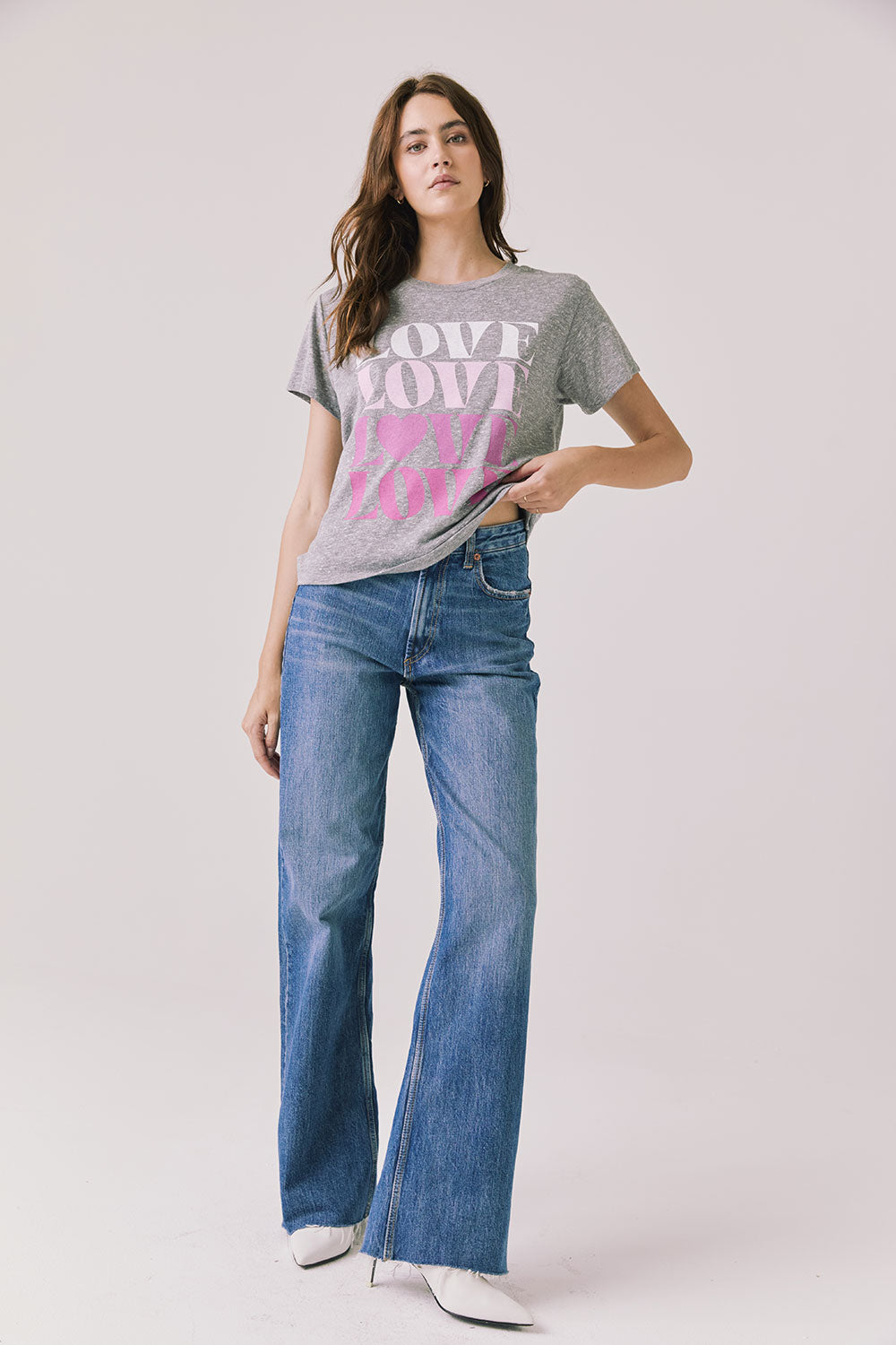 Full body view of woman wearing Chaser’s Streaky Grey Love Tee with pink text and blue jeans on a white background