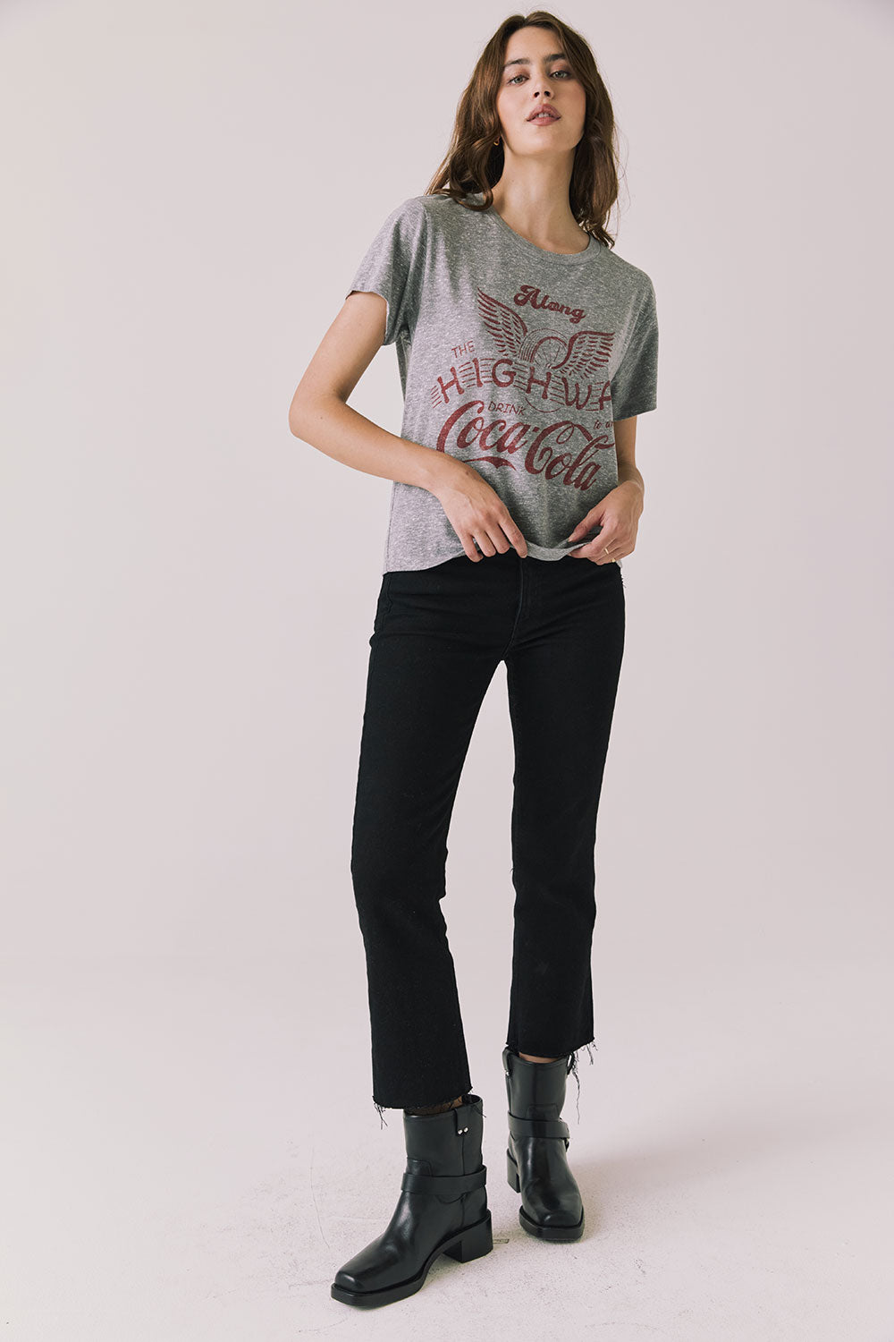 Full body view of woman wearing Chaser’s graphic Coca-Cola Highway To Anywhere Tee and black pants on a plain background