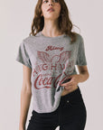 Front view of woman wearing Chaser’s graphic Coca-Cola Highway To Anywhere Tee with black pants on a plain background