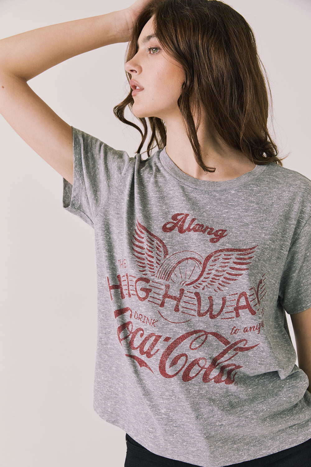Front view of woman wearing Chaser’s graphic Coca-Cola Highway To Anywhere Tee with black pants on a plain background