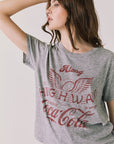 Front view of woman wearing Chaser’s graphic Coca-Cola Highway To Anywhere Tee with black pants on a plain background