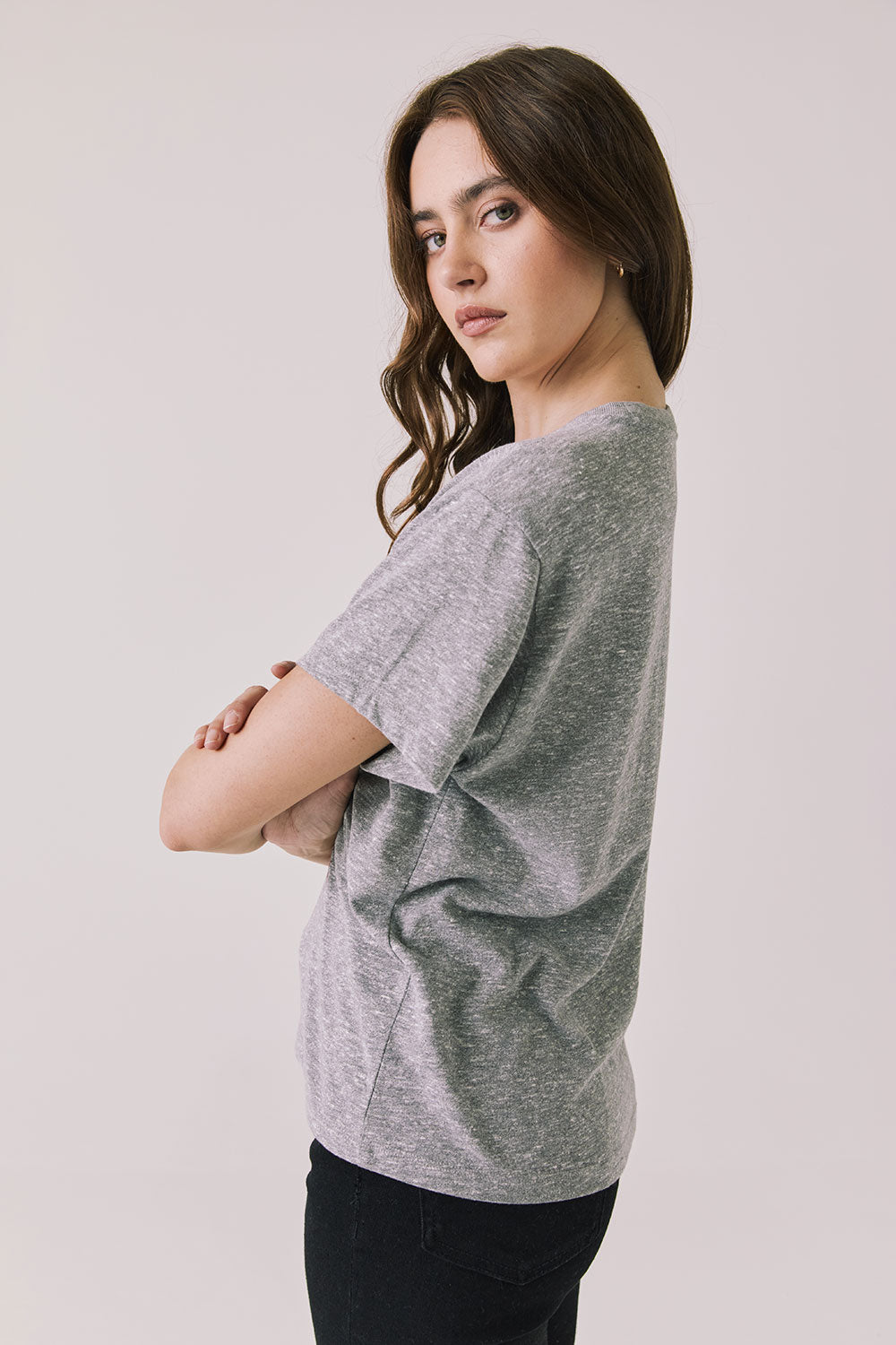 Side view of woman wearing Chaser’s graphic Coca-Cola Highway To Anywhere Tee with black pants on a plain background