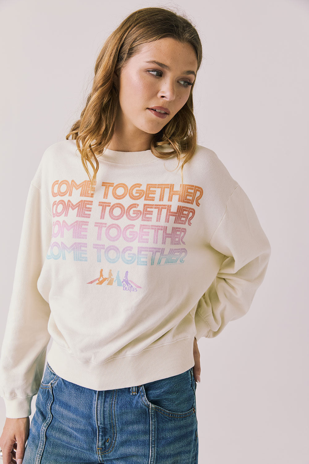 Front view of woman wearing Chaser’s The Beatles Come Together Starry White Long Sleeve with ‘COME TOGETHER’ text in rainbow colors on a plain background