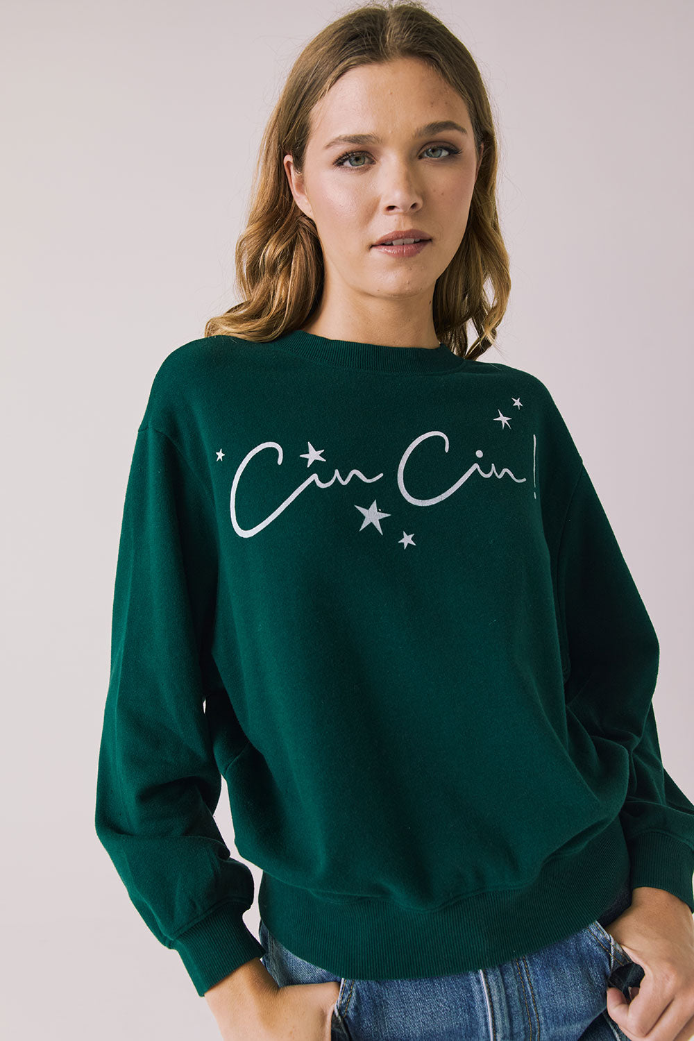 Front view of woman wearing Chaser’s green Cin Cin! Long Sleeve with “Cin Cin” text and star graphics on a plain background