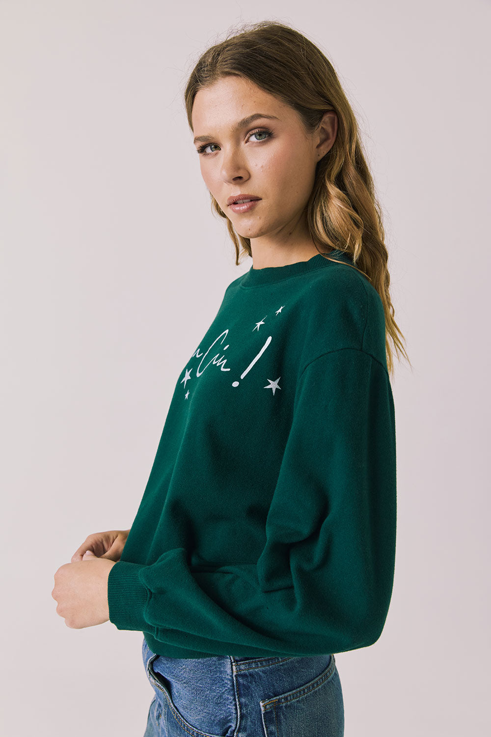 Side view of woman wearing Chaser’s green Cin Cin! Long Sleeve with “Cin Cin” text and star graphics on a plain background