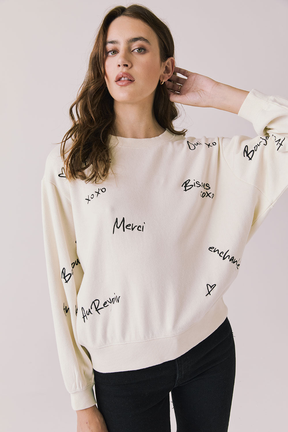 Front view of woman wearing Chaser’s Starry White French Scripts Long Sleeve with French phrases like “Merci” and “Bonjour” in black text on a white background