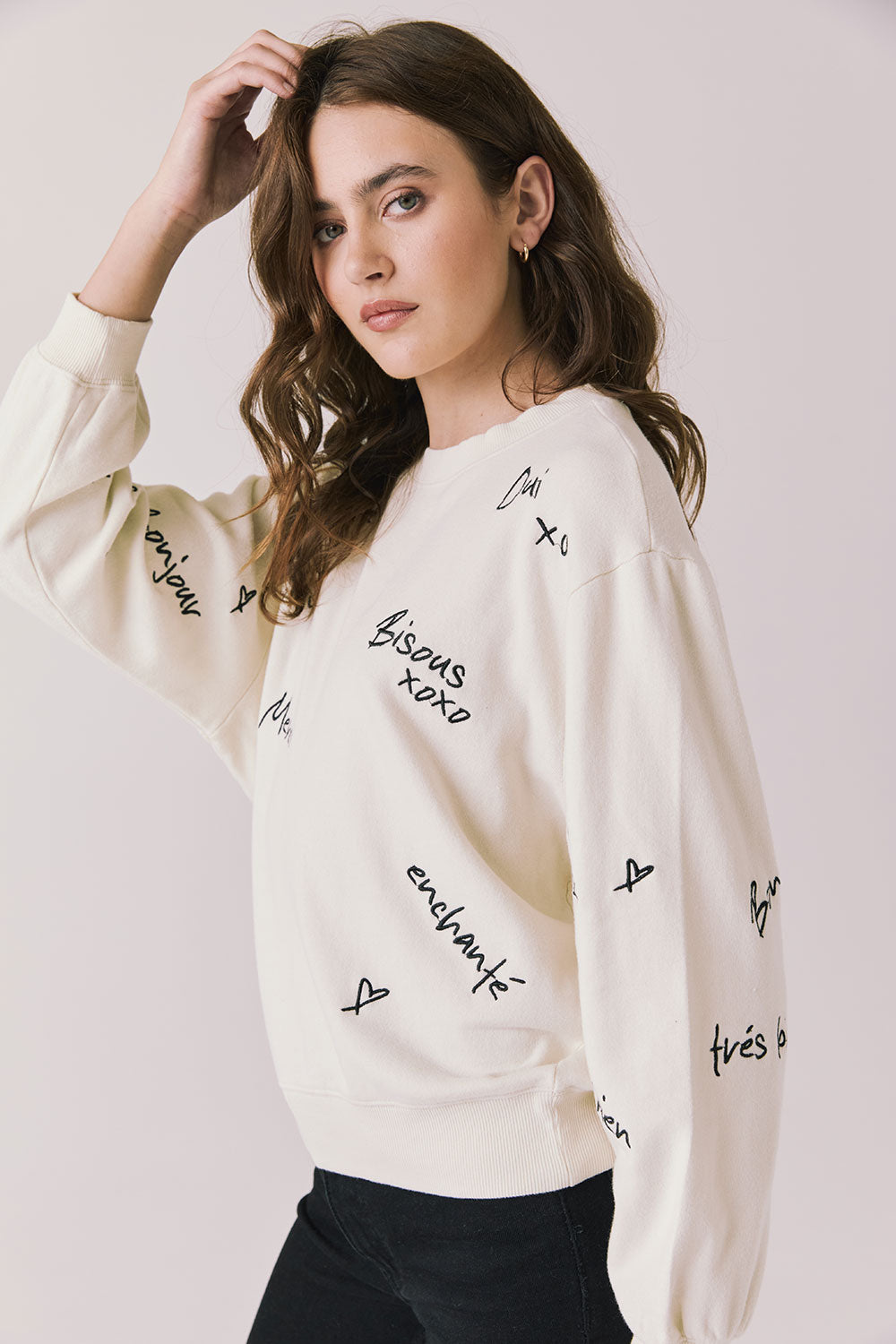 Side view of woman wearing Chaser’s Starry White French Scripts Long Sleeve with French phrases like “Merci” and “Bonjour” in black text on a white background