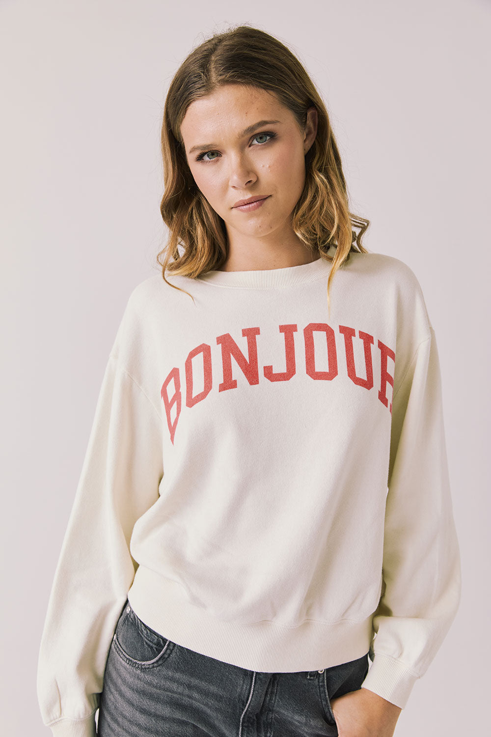 Front view of woman wearing Chaser’s starry white Bonjour Long Sleeve with ‘Bonjour’ in red text on a plain background.