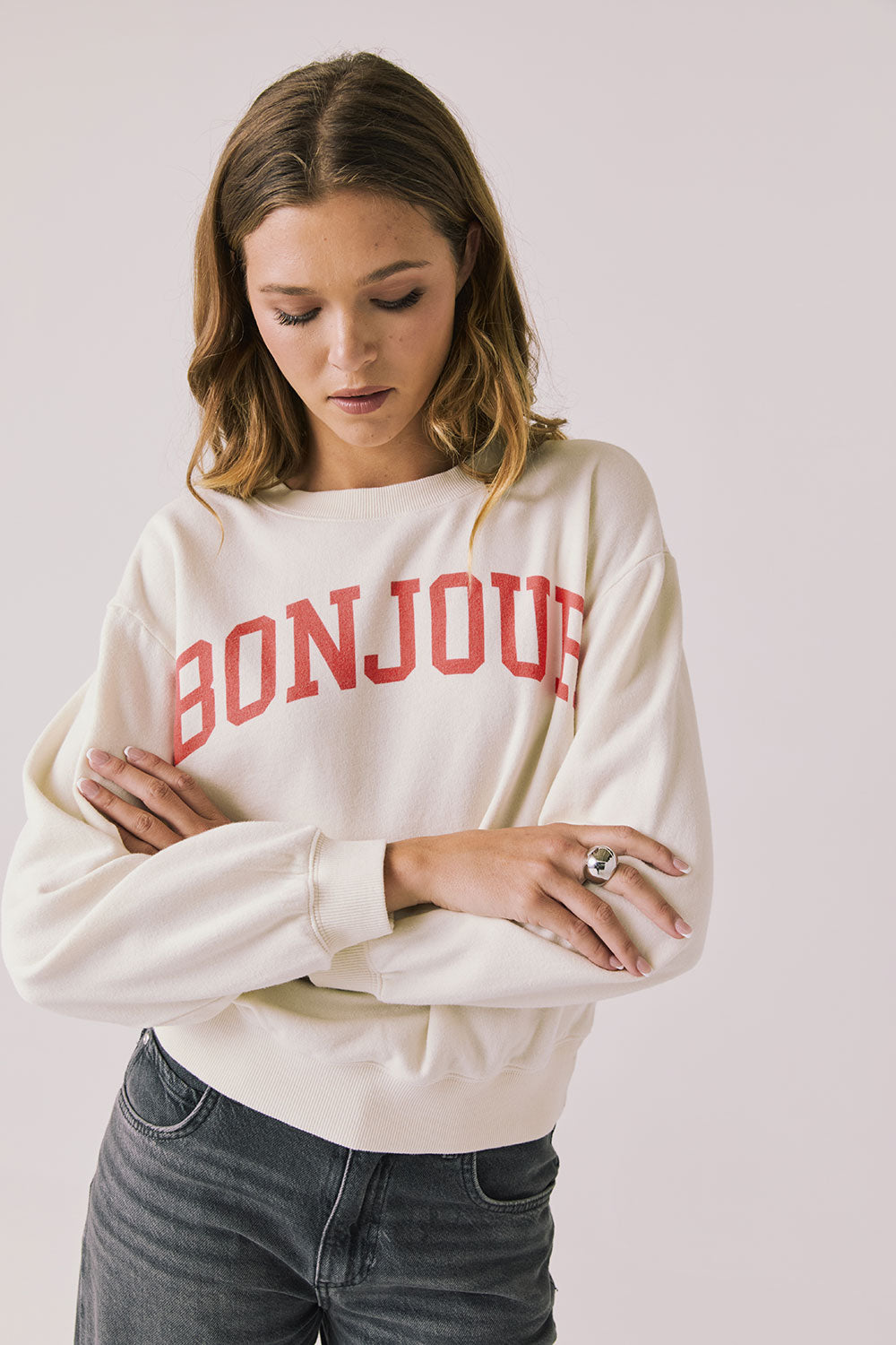 Front view of woman wearing Chaser’s starry white Bonjour Long Sleeve with ‘Bonjour’ in red text on a plain background.
