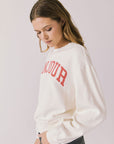 Side view of woman wearing Chaser’s starry white Bonjour Long Sleeve with red ‘Bonjour’ text visible on the front on a plain background.