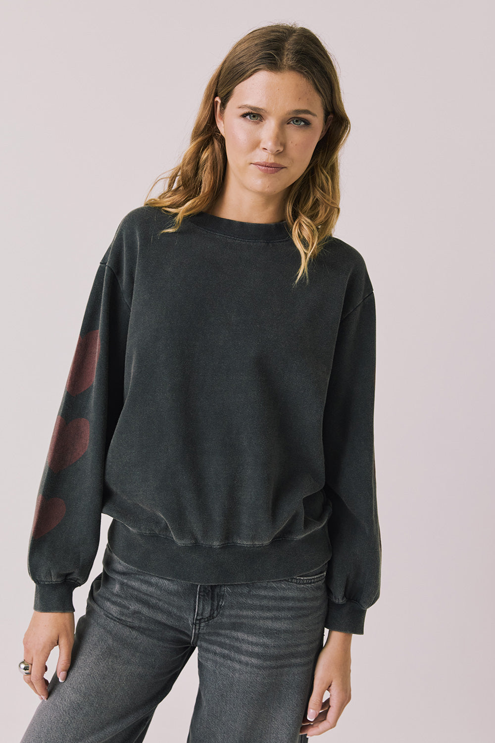 Front view of woman wearing Chaser’s Red Hearts Black Mineral Wash Long Sleeve with red hearts on the sleeves on a light pink background