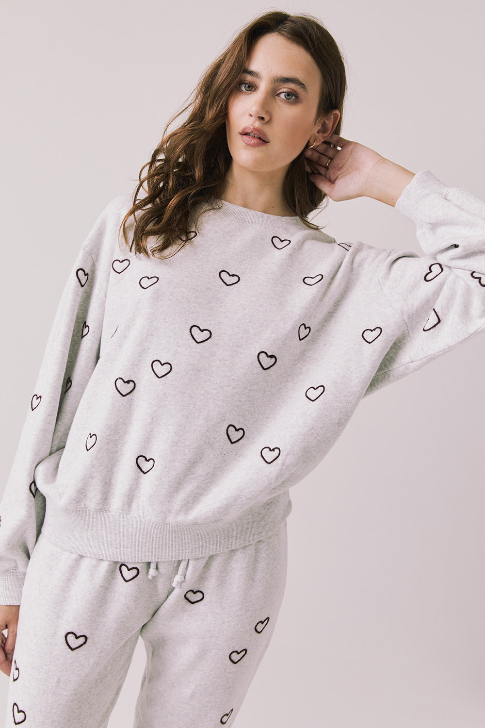 Front view of woman wearing Chaser’s light grey Tossed Hearts Long Sleeve with allover heart patterns on a white background