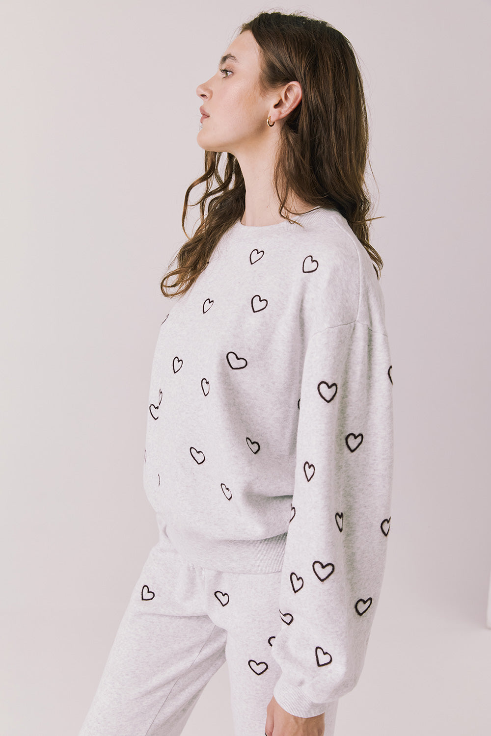 Side view of woman wearing Chaser’s light grey Tossed Hearts Long Sleeve with heart prints on a white background