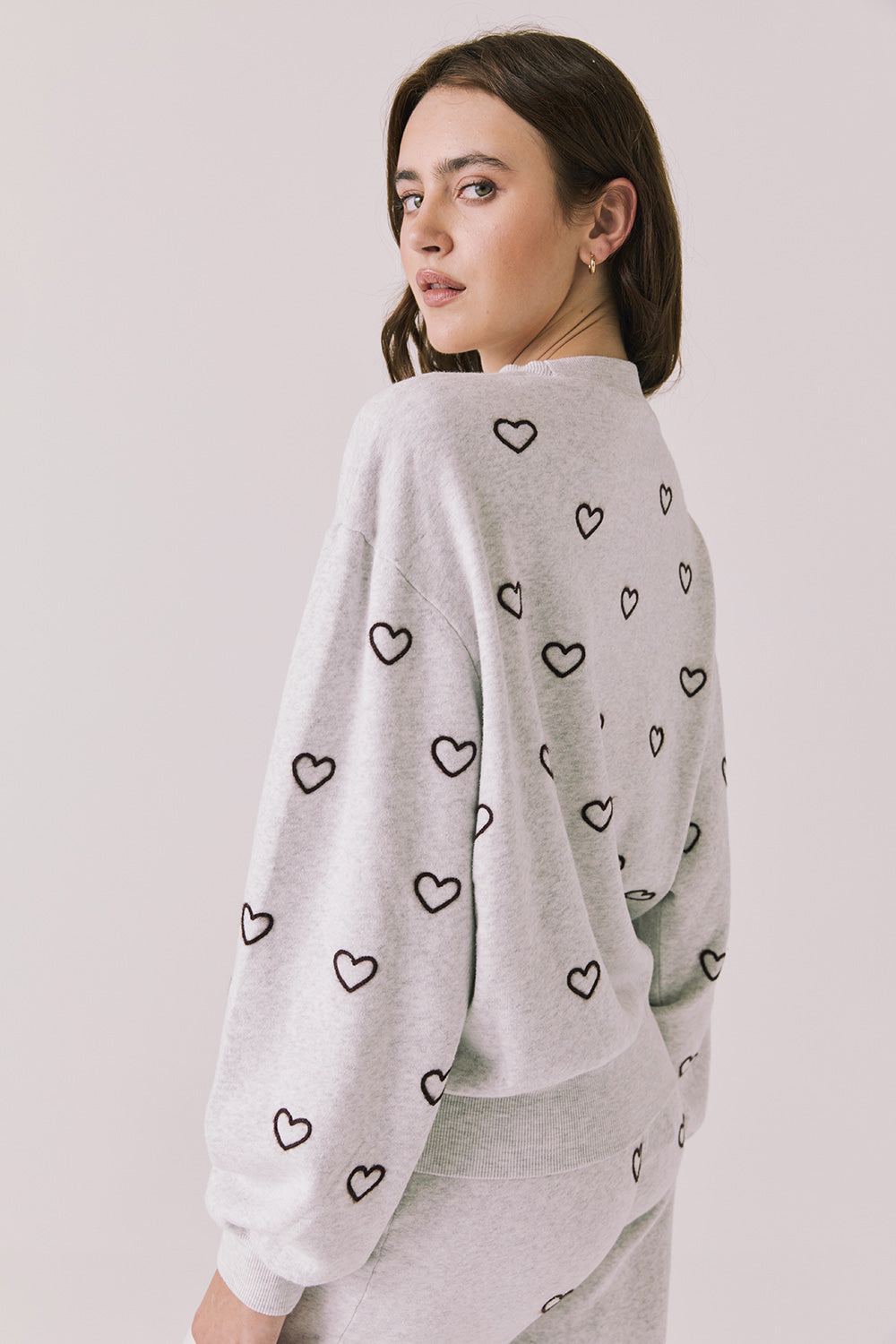 Back view of woman wearing Chaser’s light grey Tossed Hearts Long Sleeve with heart design on a white background