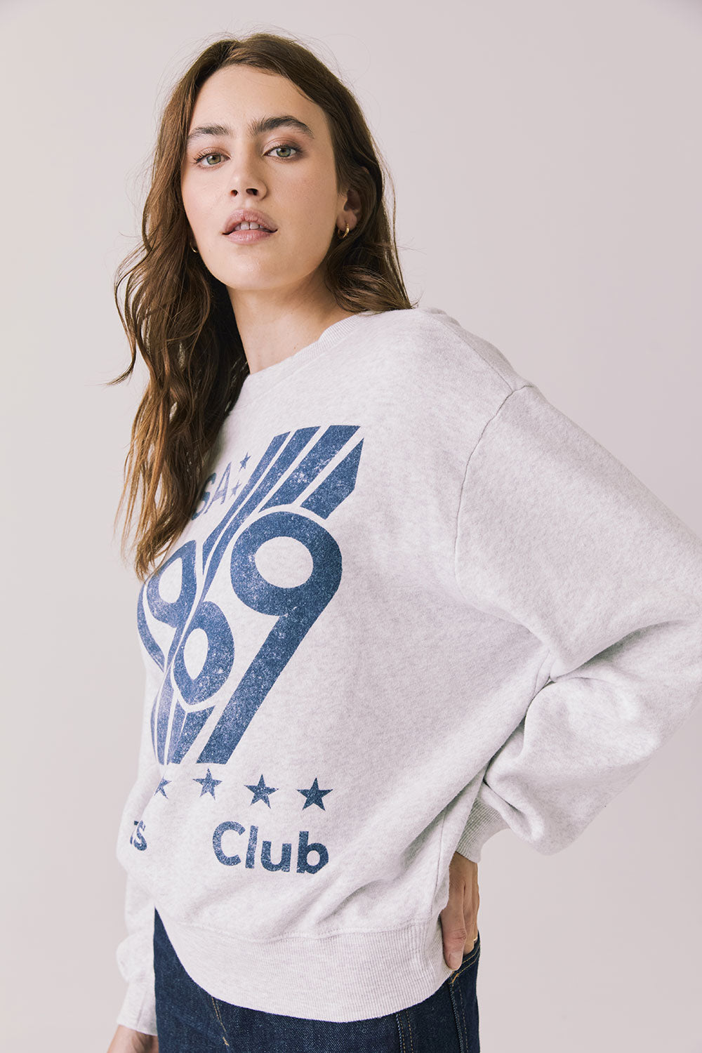 Side view of woman wearing Chaser’s light grey USA Sports Club Long Sleeve with blue USA 1969 print on a white background