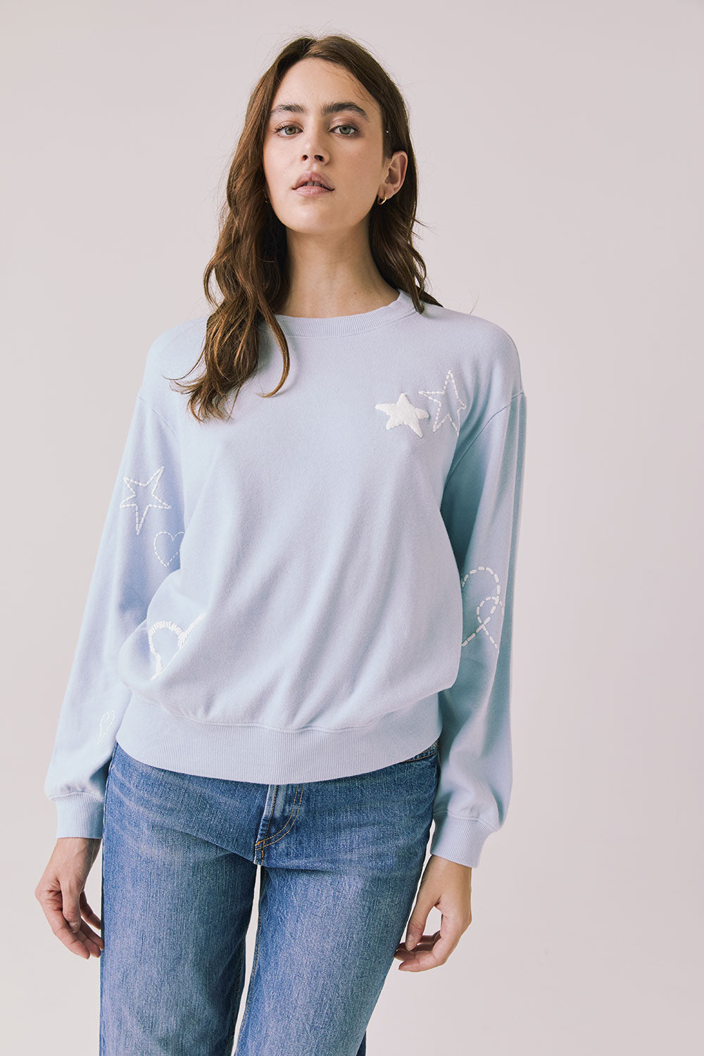 Front view of woman wearing Chaser’s Light Blue Love Stars Stitches Pullover Long Sleeve with star designs on a plain background