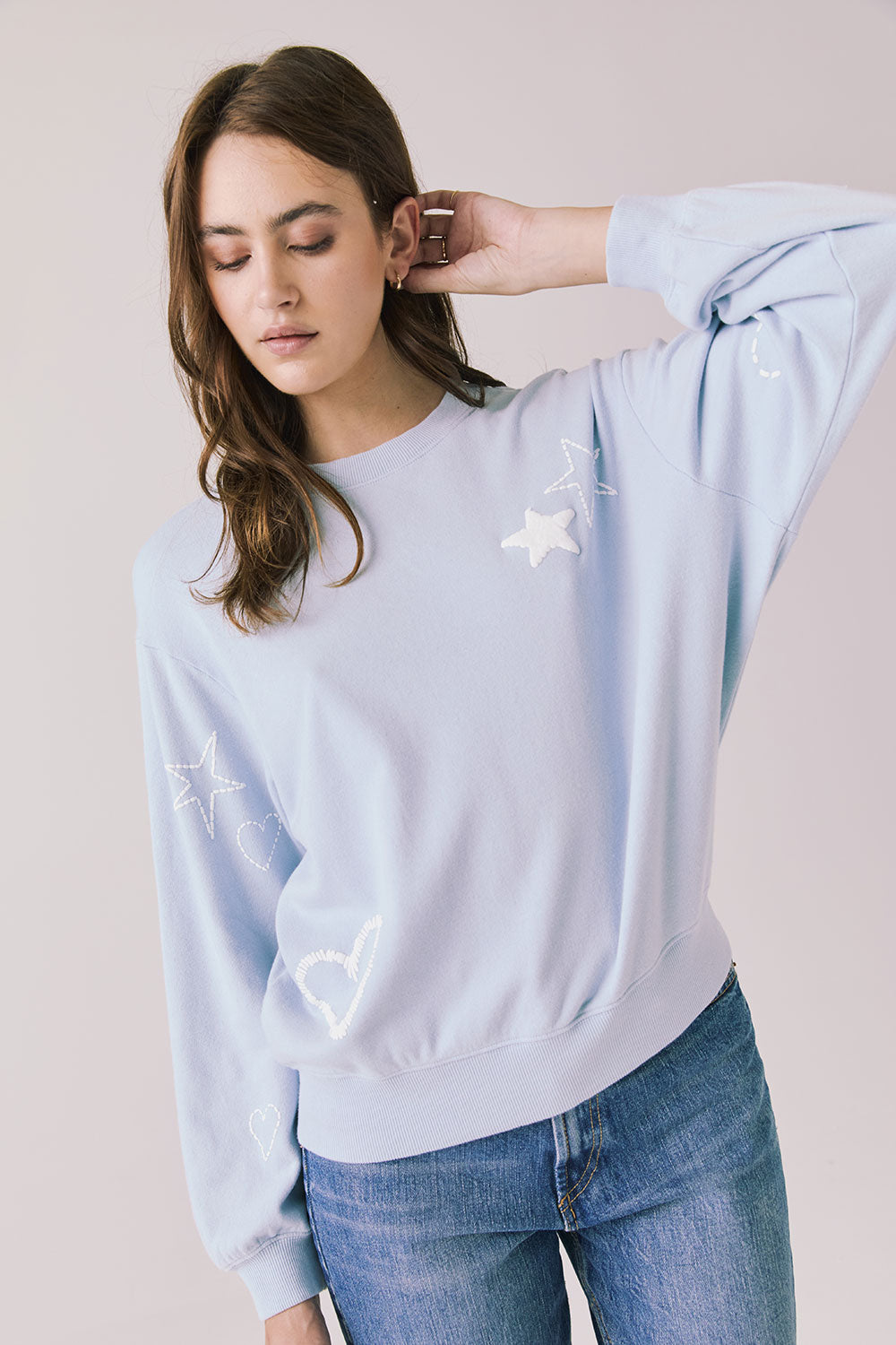 Front view of woman wearing Chaser’s Light Blue Love Stars Stitches Pullover Long Sleeve with star designs on a plain background