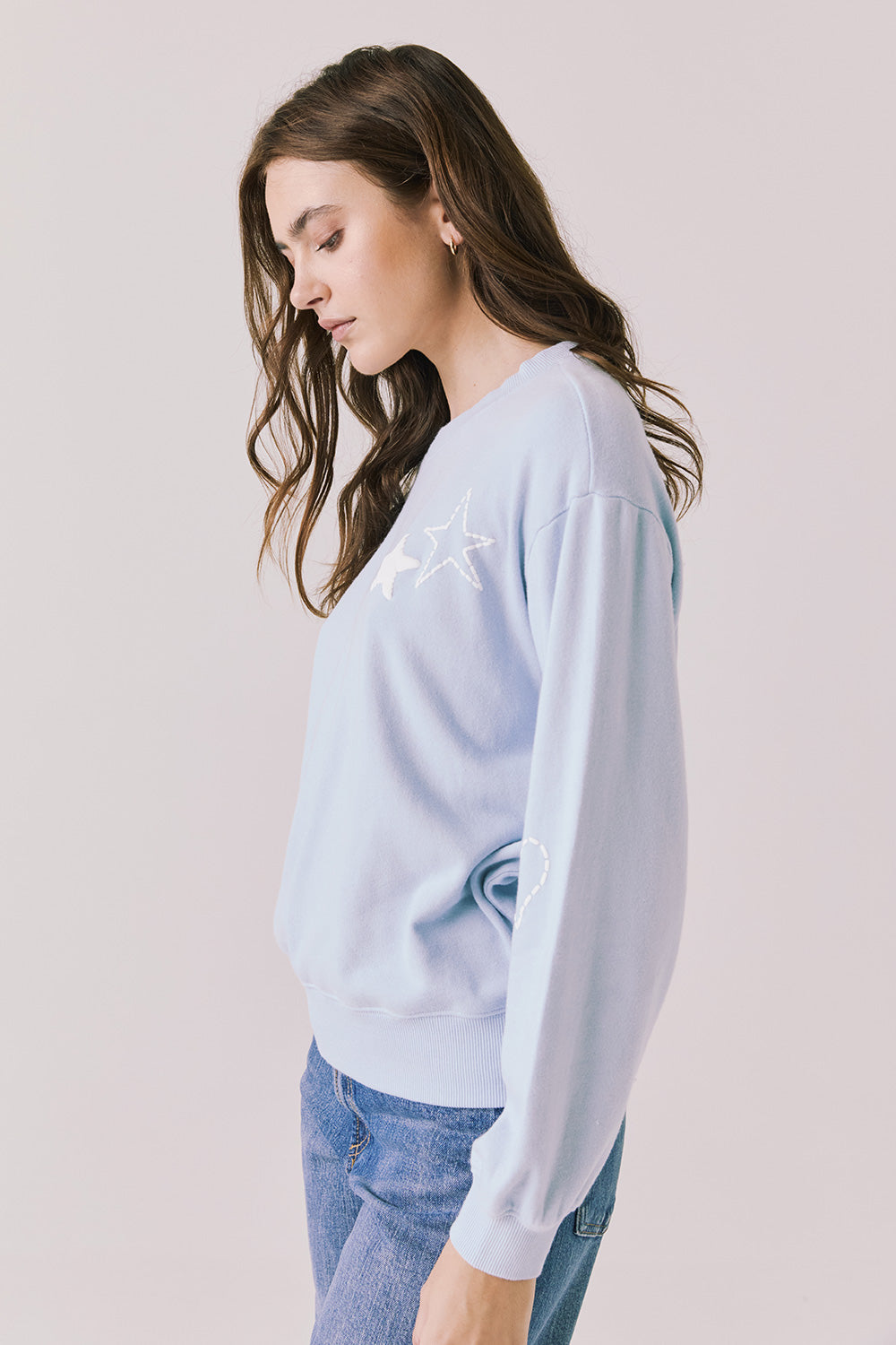 Side view of woman wearing Chaser’s Light Blue Love Stars Stitches Pullover Long Sleeve with star designs on a plain background