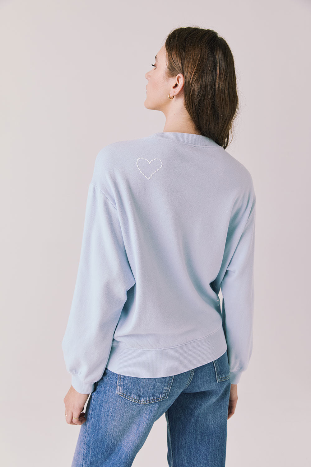 Back view of woman wearing Chaser’s Light Blue Love Stars Stitches Pullover Long Sleeve with star designs on a plain background