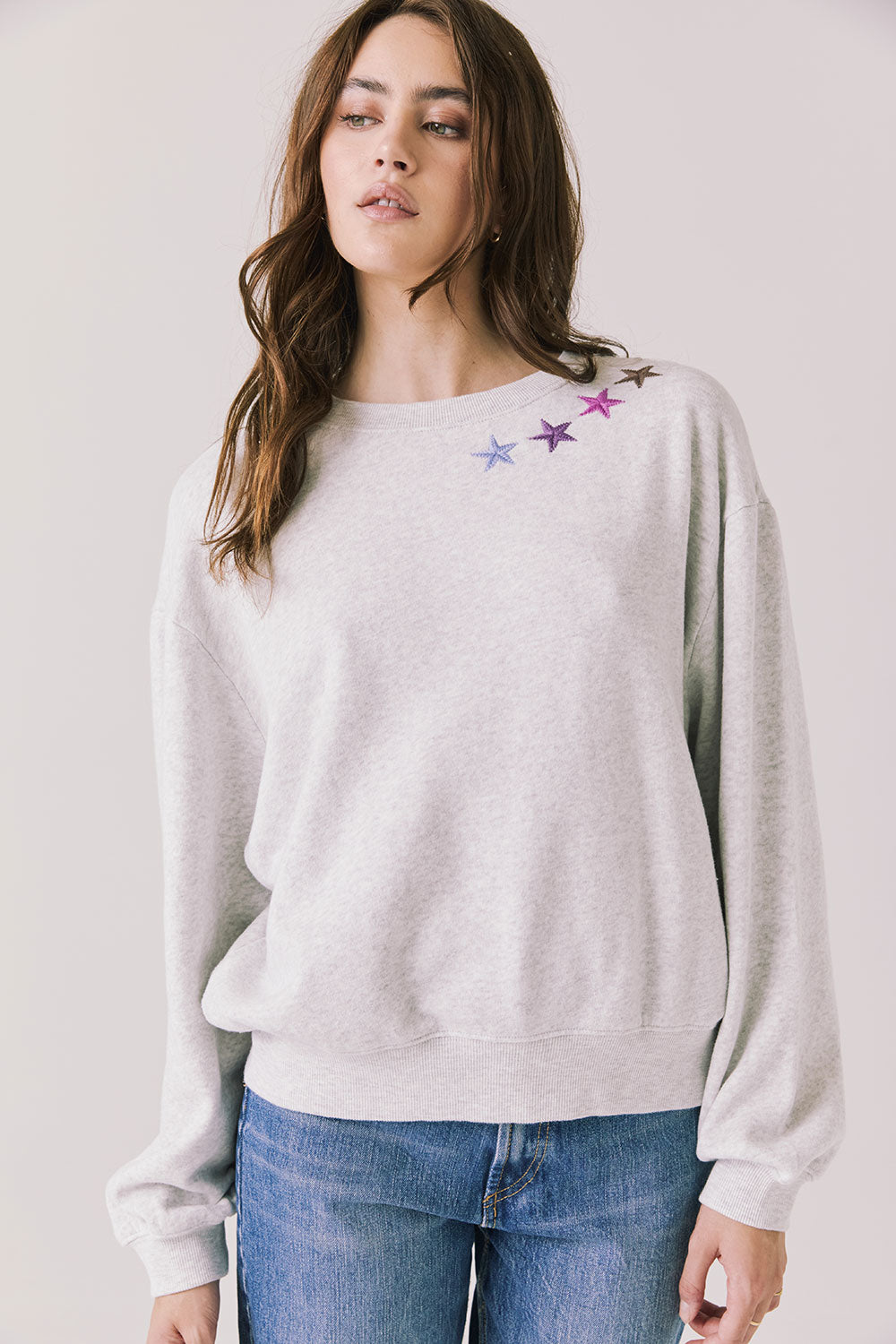 Front view of woman wearing Chaser’s Star Chainstitch Light Grey Long Sleeve with embroidered stars on a plain background