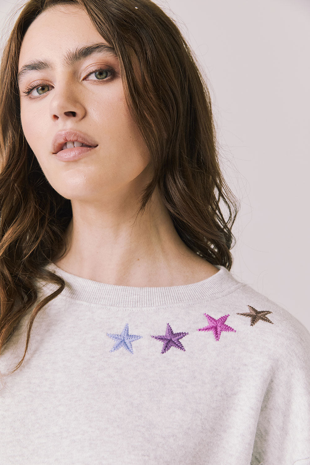 Front view of woman wearing Chaser’s Star Chainstitch Light Grey Long Sleeve with embroidered stars on a plain background
