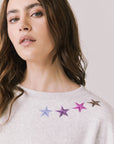 Front view of woman wearing Chaser’s Star Chainstitch Light Grey Long Sleeve with embroidered stars on a plain background
