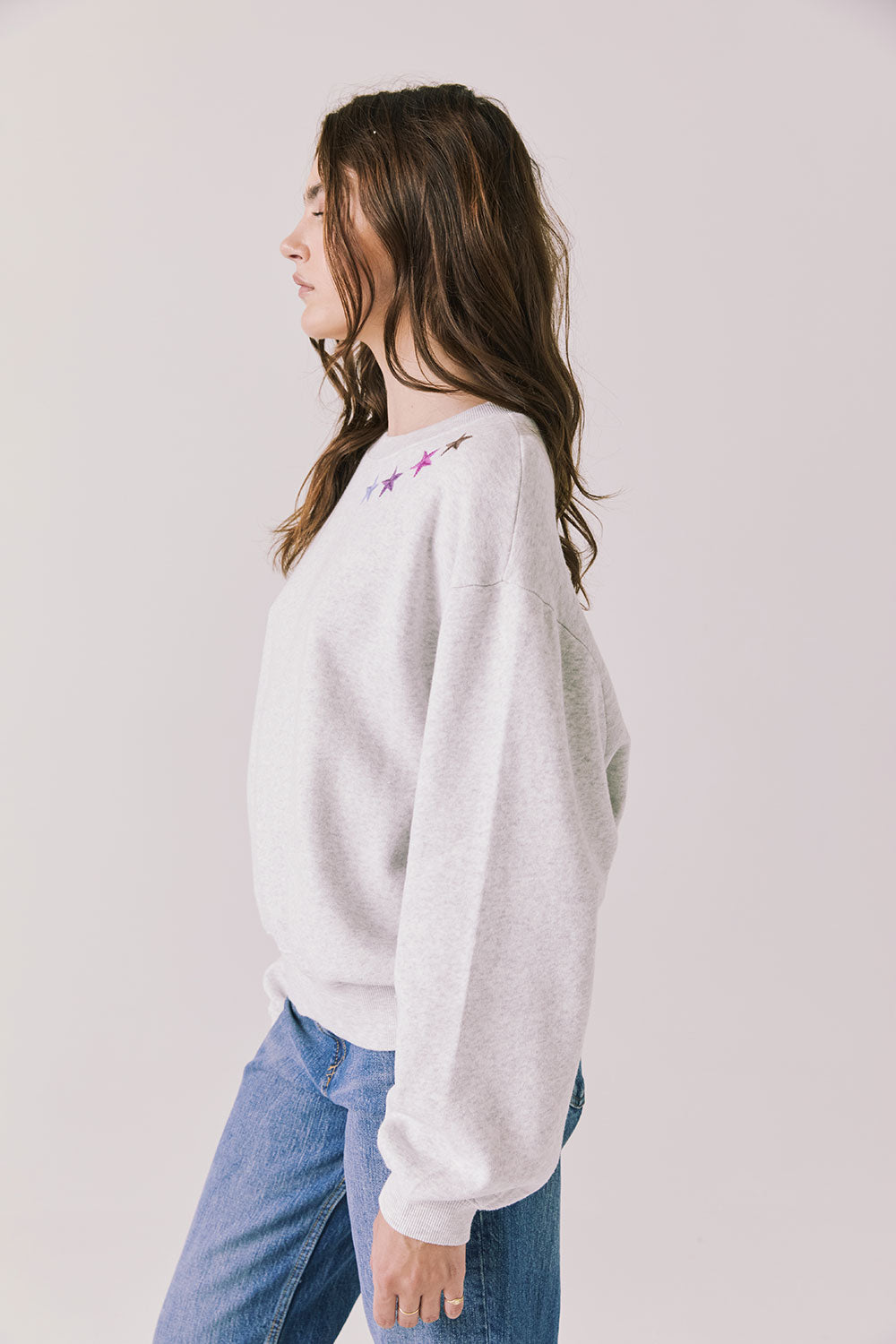 Side view of woman wearing Chaser’s Star Chainstitch Light Grey Long Sleeve on a plain background
