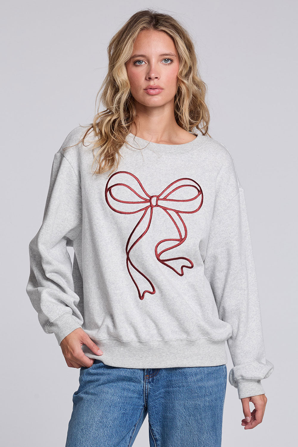 Model wearing Chaser's Merry Bow Pullover in Heather Grey with oversized red bow artwork, front view