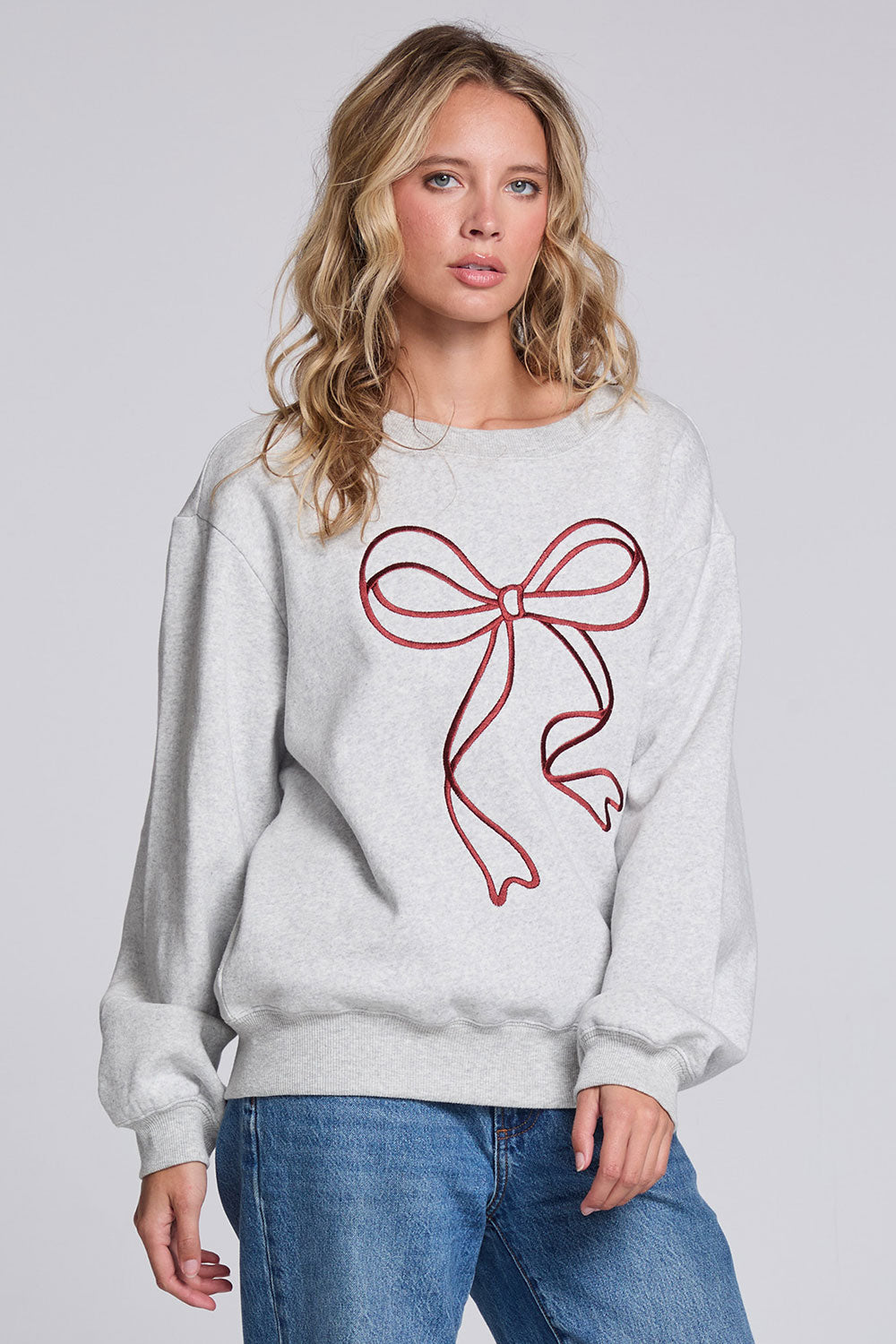 Model wearing Chaser's Merry Bow Pullover in Heather Grey with oversized red bow artwork, angled view