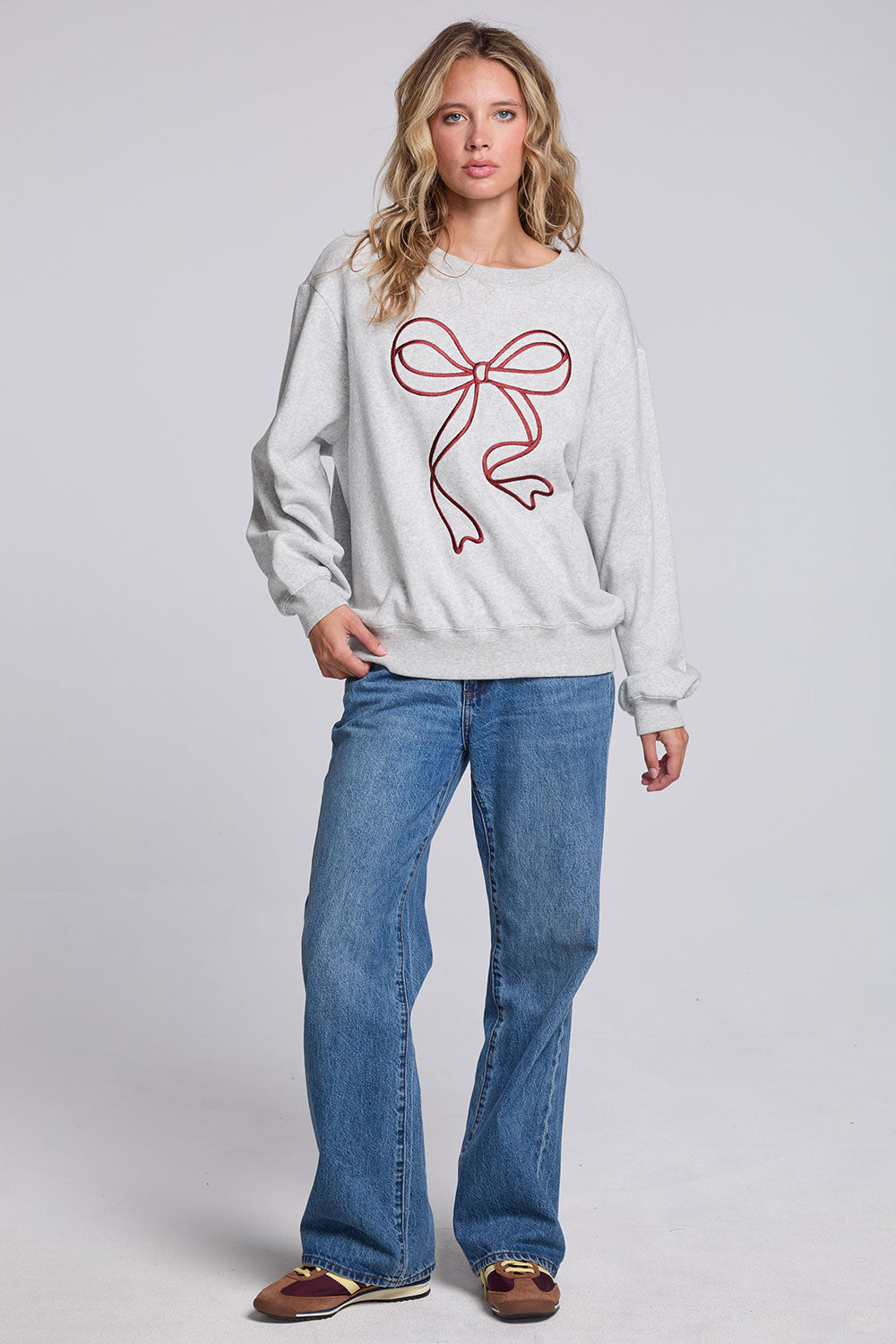 Model wearing Chaser's Merry Bow Pullover in Heather Grey with oversized red bow artwork, full-body view