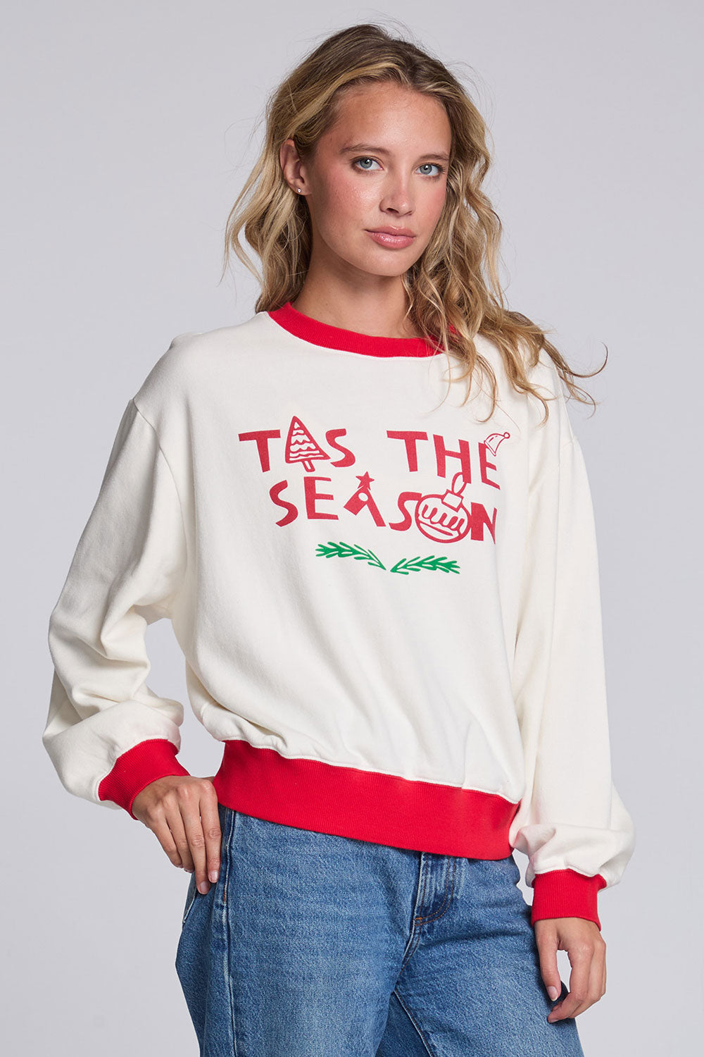 Model wearing Chaser's 'Tis the Season Pullover in Whisper White with red and green 'Tis the Season lettering and red trim, angled view