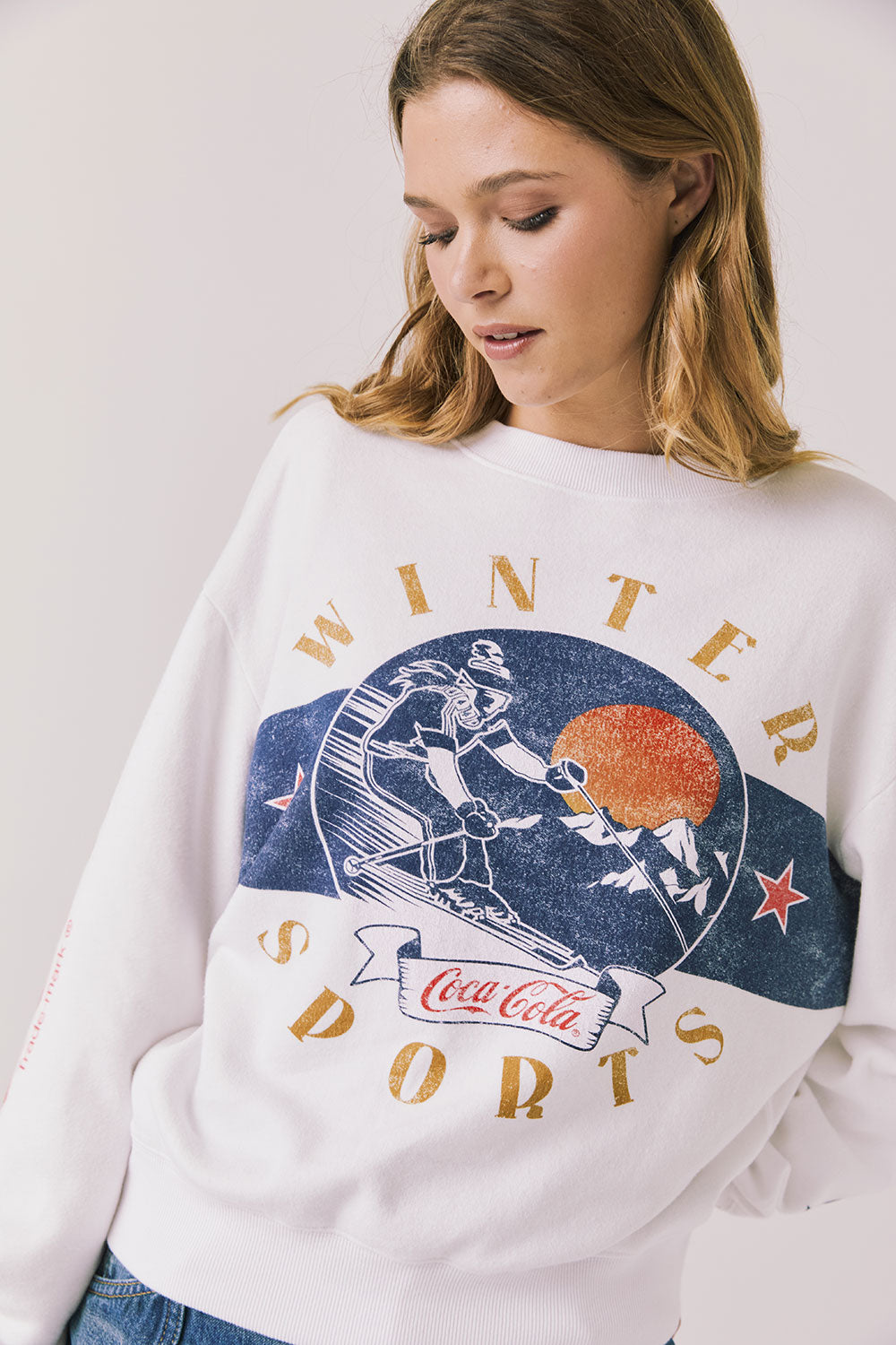 Front view of woman wearing Chaser’s white Coca-Cola Winter Sports Long Sleeve with vintage-inspired graphic design on a plain background