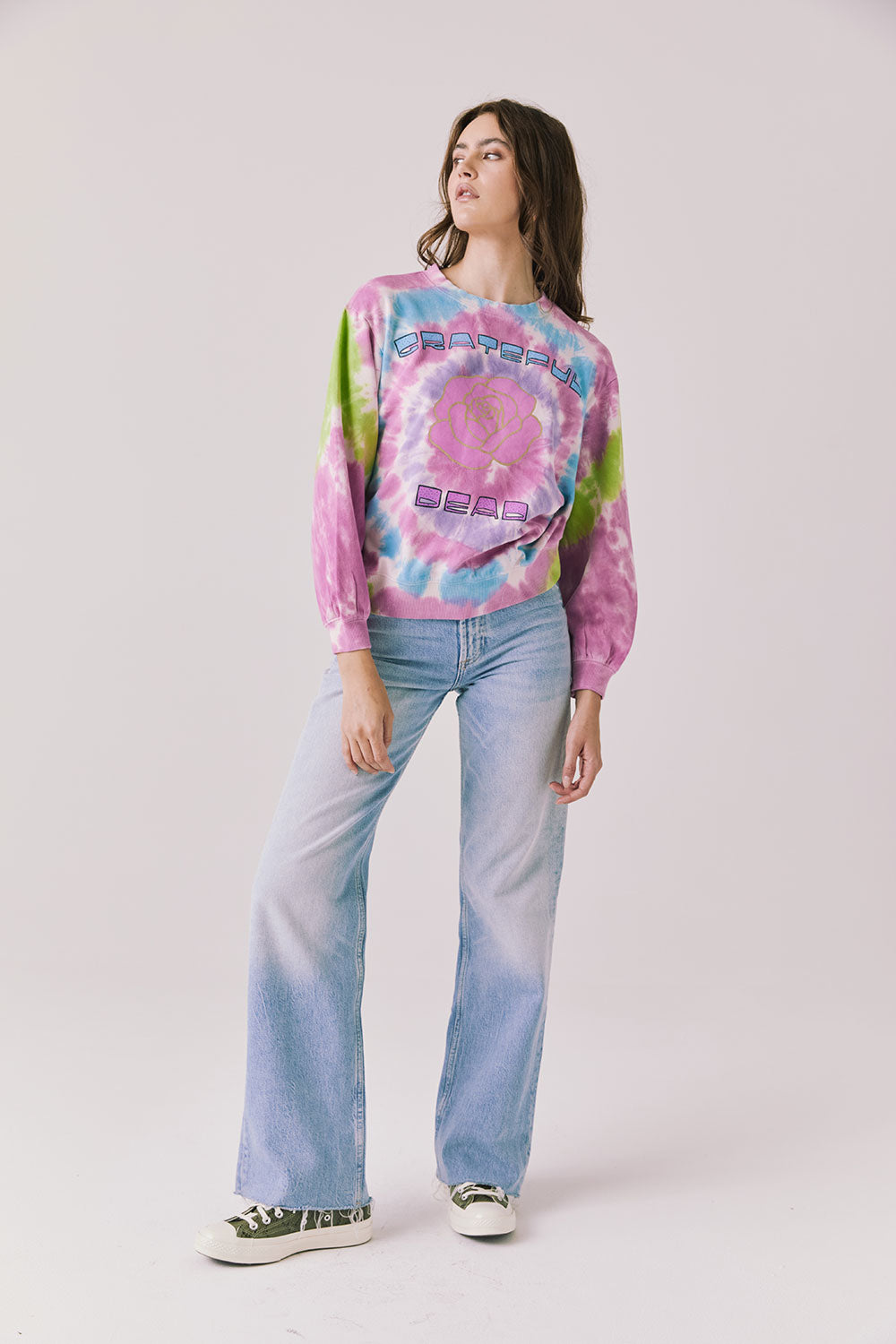  Full body view of woman wearing Chaser’s Grateful Dead Rose Logo Long Sleeve tie-dye top with blue jeans on a plain background