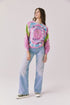  Full body view of woman wearing Chaser’s Grateful Dead Rose Logo Long Sleeve tie-dye top with blue jeans on a plain background