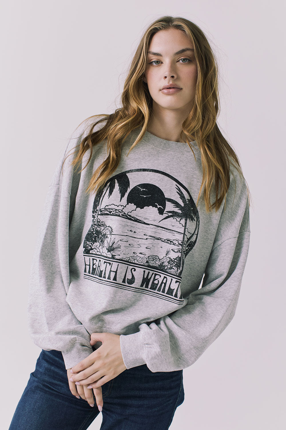 Front view of a woman wearing Chaser's gray Health Is Wealth Long Sleeve with a graphic design on a plain background