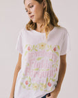Front view of woman wearing Chaser’s The Beatles Strawberry Fields Forever White Tee with floral and pink text design on a plain background