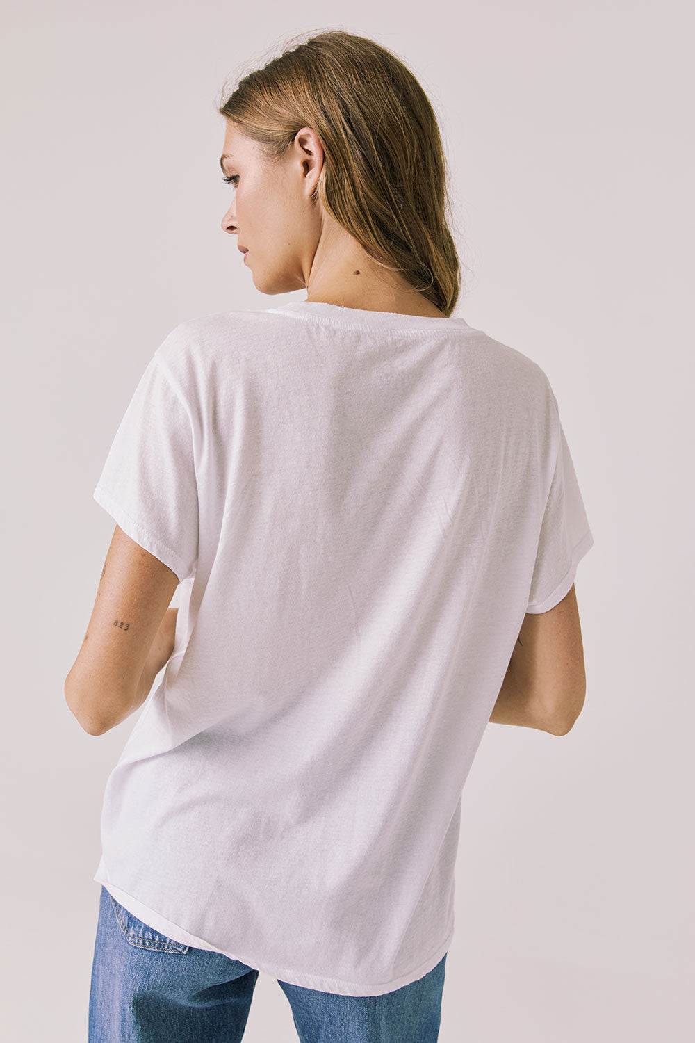 Back view of woman wearing Chaser’s The Beatles Strawberry Fields Forever White Tee on a plain background