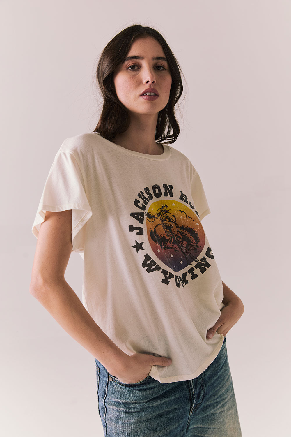 Side view of model wearing the Jackson Hole Sunset Tee in white with scenic Western graphic with graphic design on a plain background