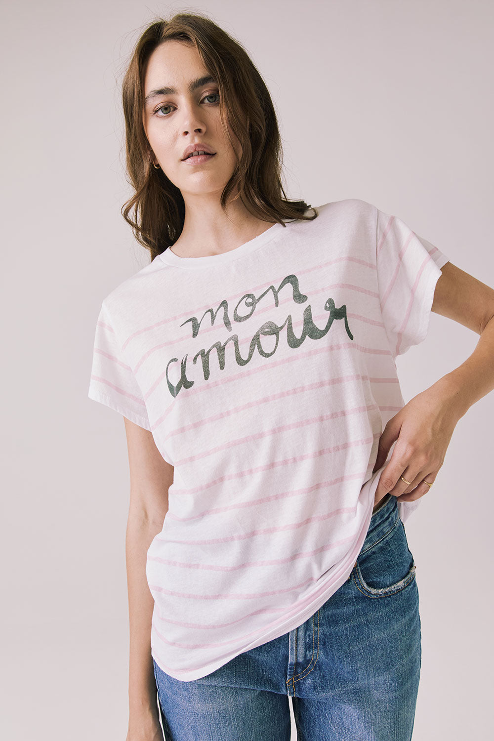 Front view of woman wearing Chaser’s white Mon Amour Stripe Tee with “mon amour” French text and light pink stripes on a plain background