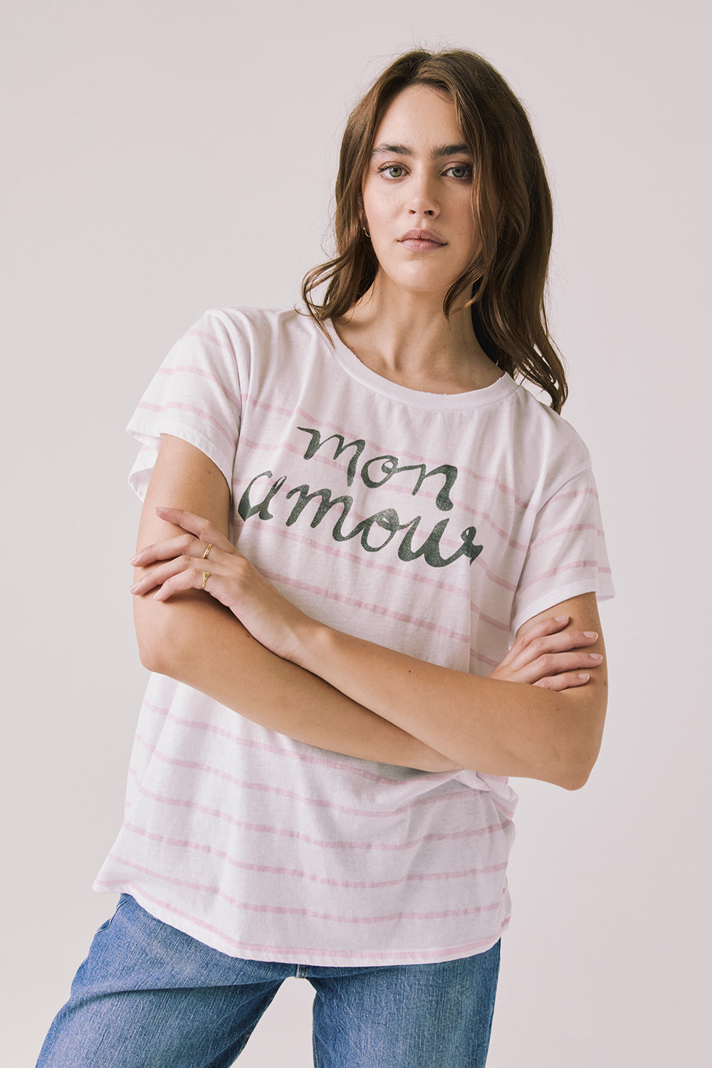 Front view of woman wearing Chaser’s white Mon Amour Stripe Tee with “mon amour” French text and light pink stripes on a plain background
